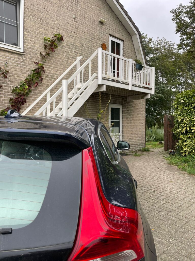 Parkeerplaats naast het woonhuis met poort richting praktijk op de achtergrond.
